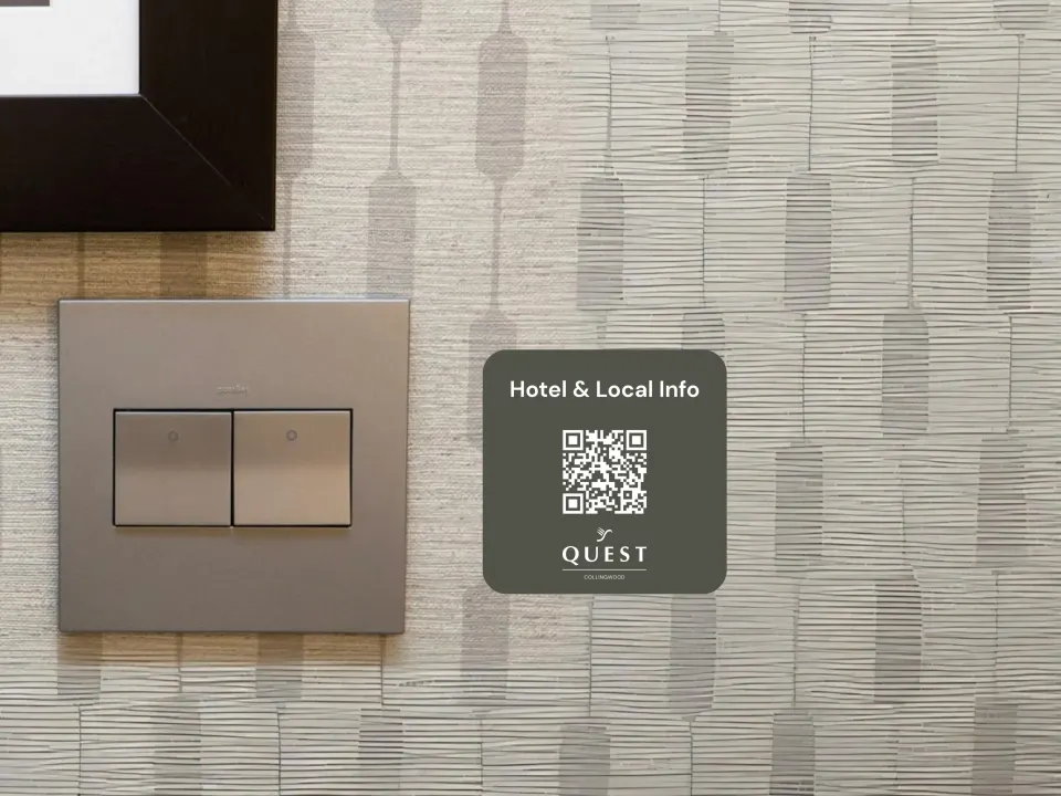 A small square Quest “Hotel & local info” QR sticker on a hotel room wall beside the light switches